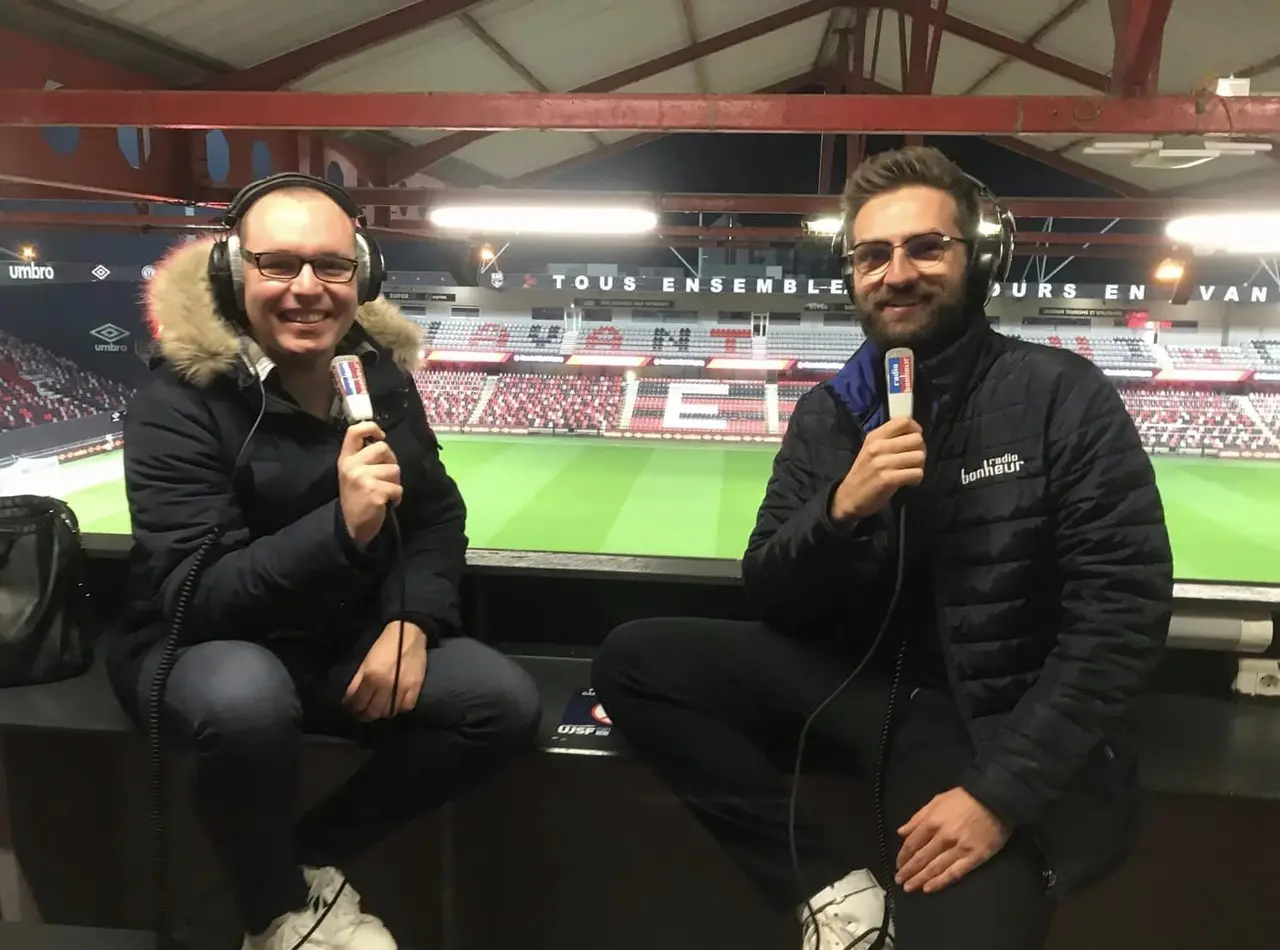 Deux commentateurs en tribune, casque sur les oreilles et micro en main, dans le stade de Guingamp